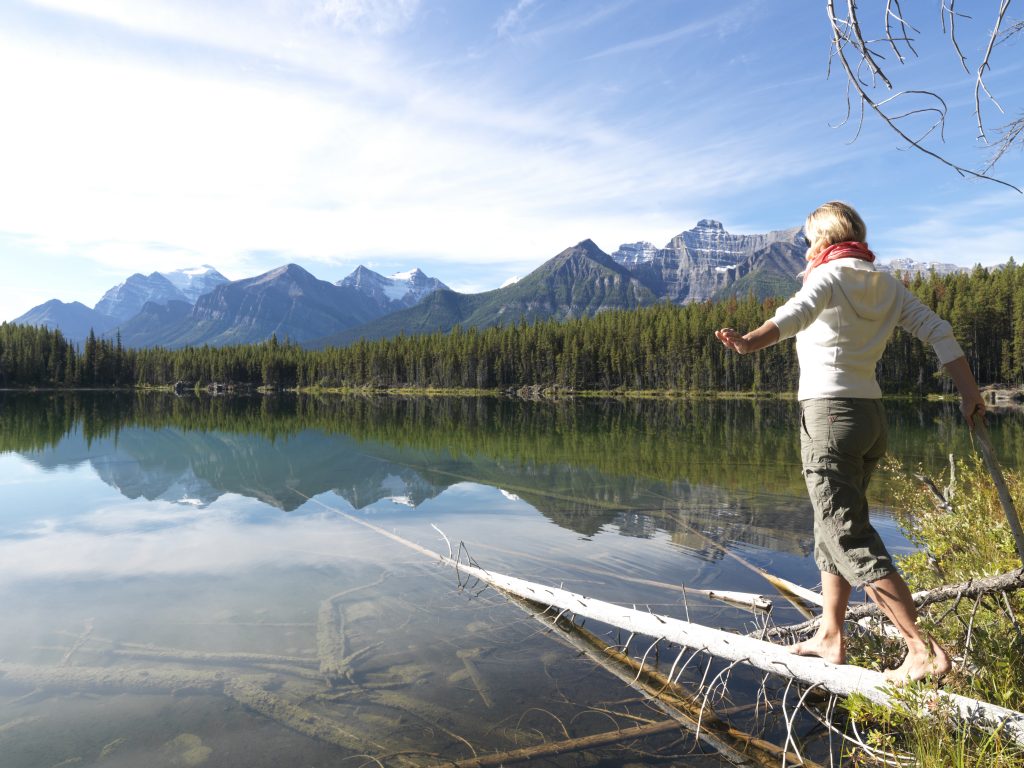 A woman practicing her balance on a log over a lake