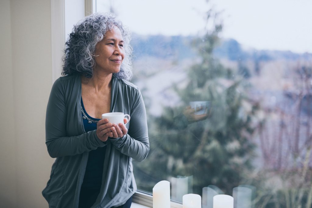 A woman holding a cup and gazing out the window